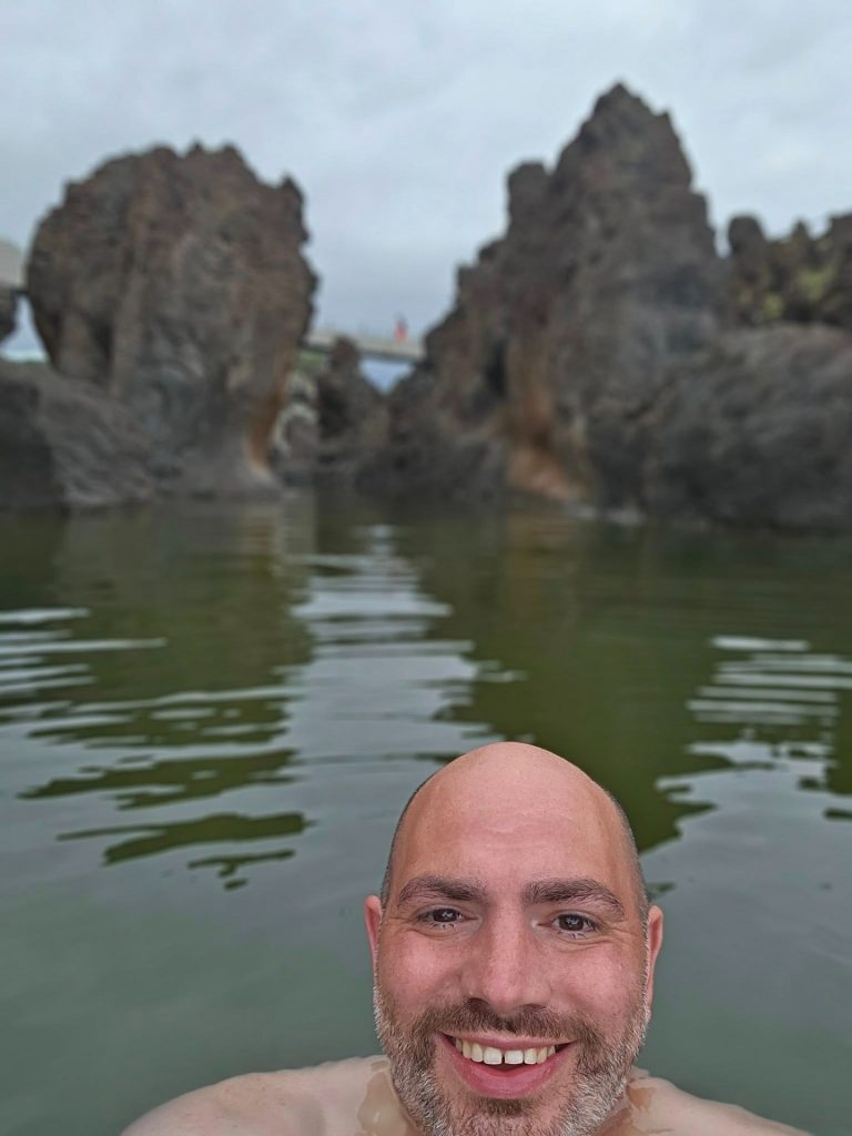 Zwemselfie in de vulkanische natuurbaden van Porto Moniz op een bewolkte avond.