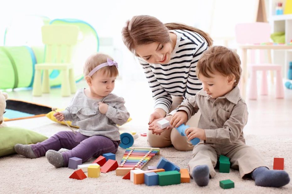 Oppas die samen met twee jonge kinderen speelt met blokken.