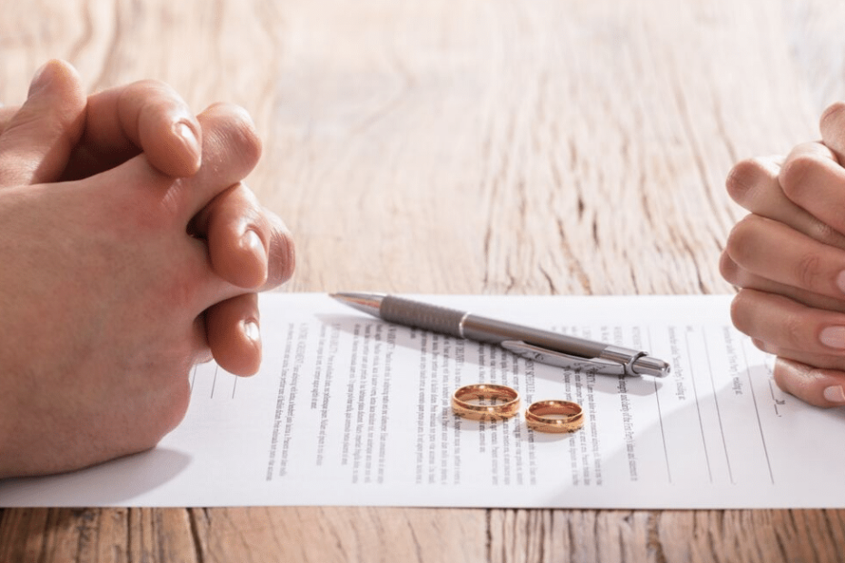 Handen gevouwen boven scheidingscontract en trouwringen, symbool voor online scheiden.