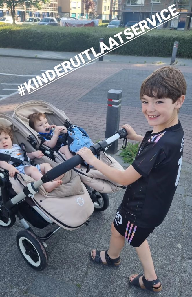 Alleenstaande vader met zoon die tweeling in een buggy voortduwt.