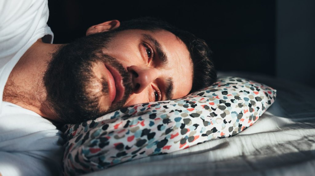 Verdrietige man alleen in bed – reflectie van emotionele schade en het gevoel van verlatenheid na een breuk.