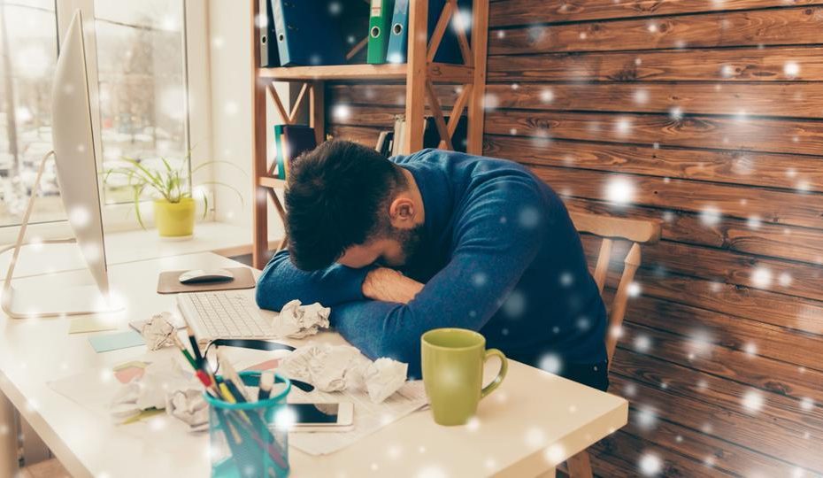 Man met winterdip slapend op bureau vol papierwerk.