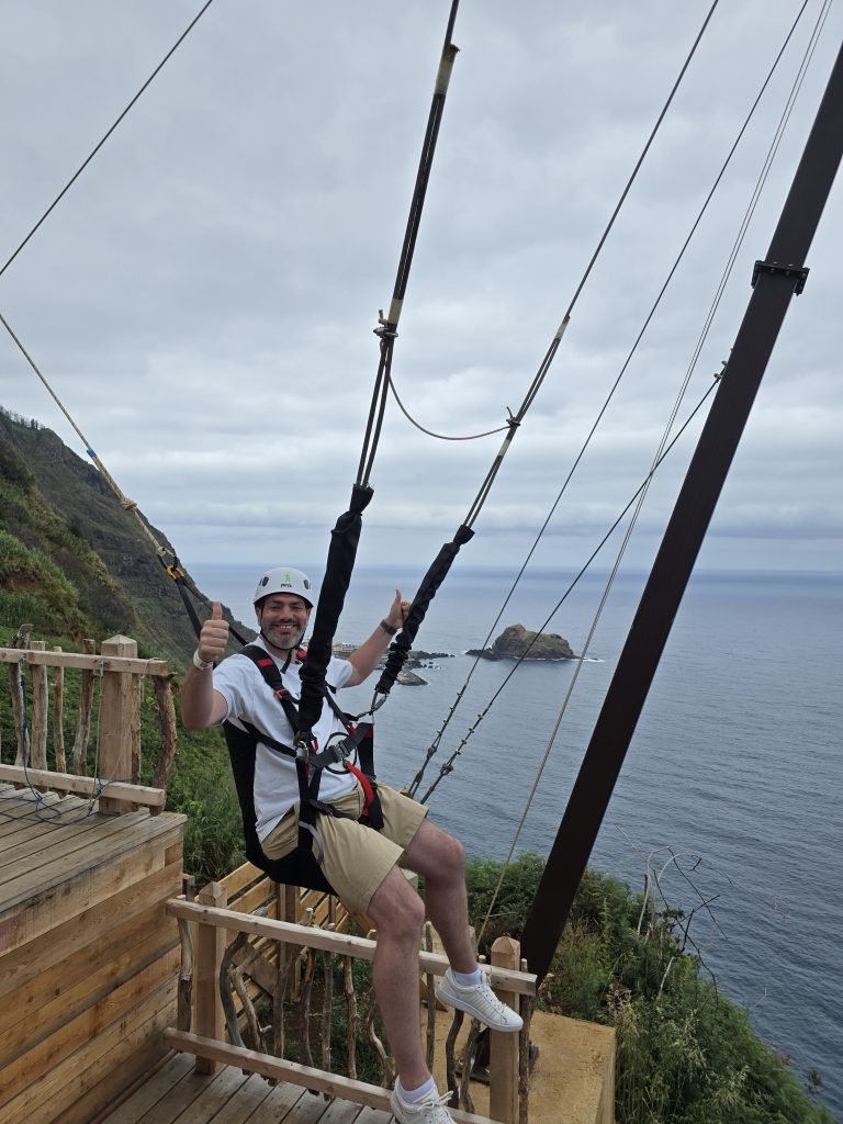 Rinaldo glimlacht met duimen omhoog op de zipline over de kliffen bij Porto Moniz.