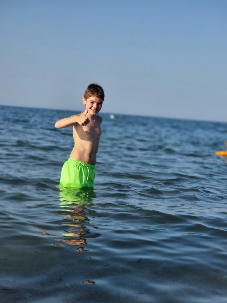 Alessio geniet van de zee en geeft een duim omhoog tijdens de vakantie.