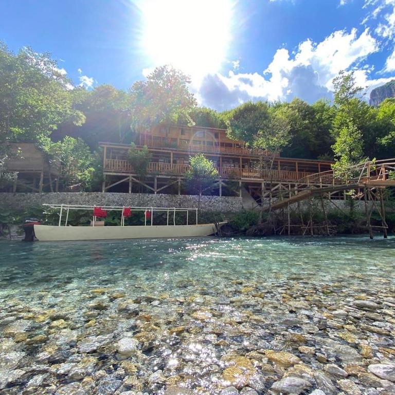 Houten lodge aan rivier met helderblauw water in Albanië, zonlicht door bomen – reisblog Albanië
