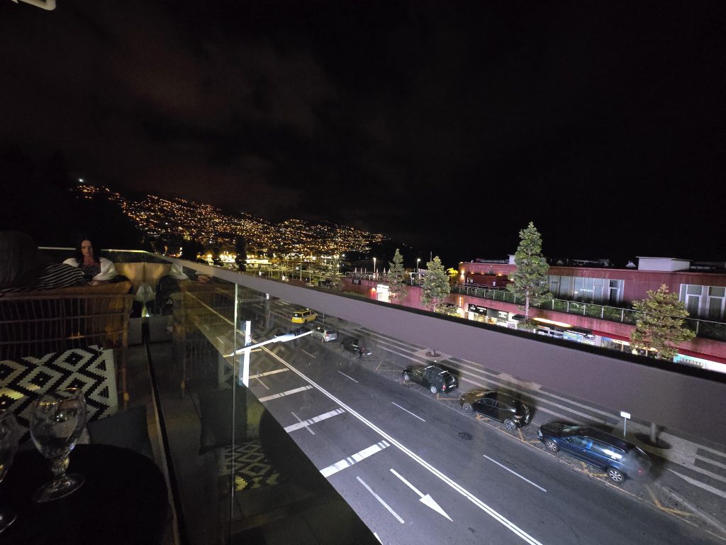 Uitzicht vanaf een rooftopbar over de verlichte heuvels van Funchal tijdens de avond.